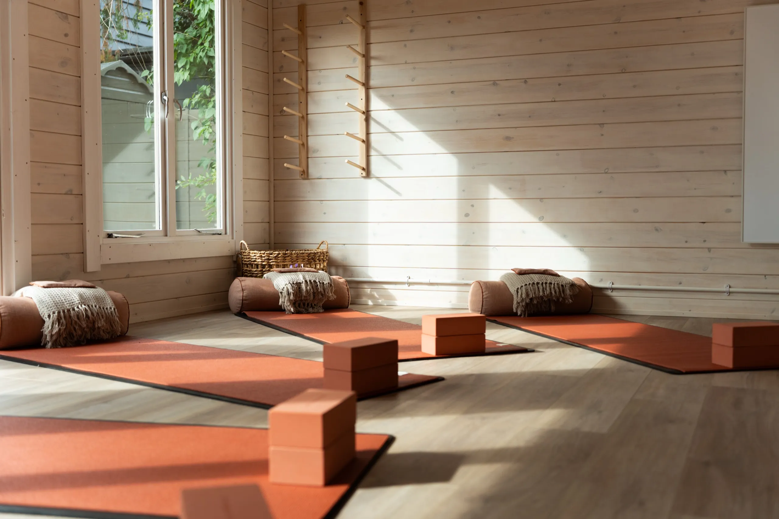 Sunlight falling across terracotta yoga mats, bolsters and blocks in the wooden garden studio